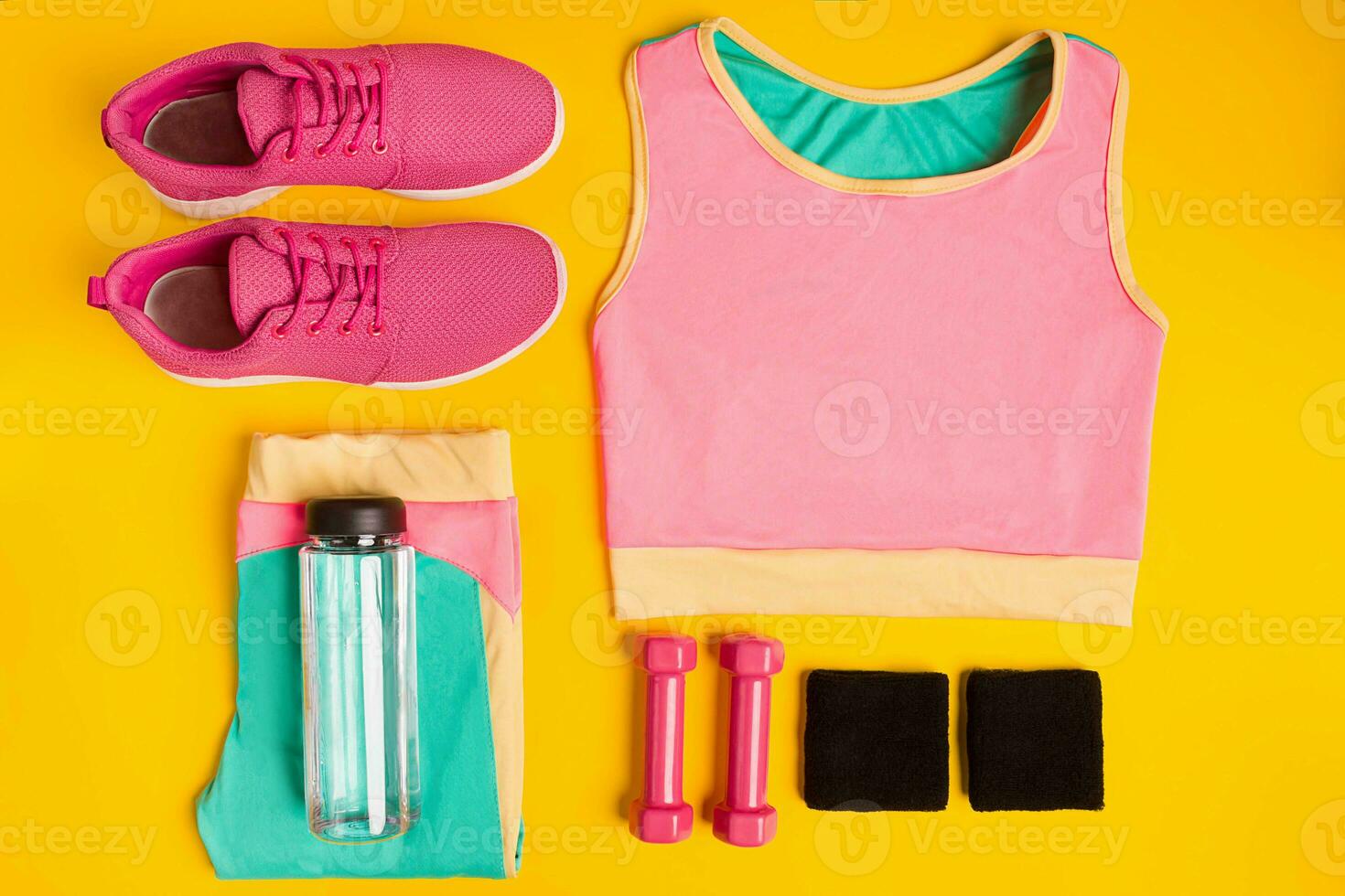 Fitness accessories on yellow background. Sneakers, bottle of water, dumbbells and sport top. photo