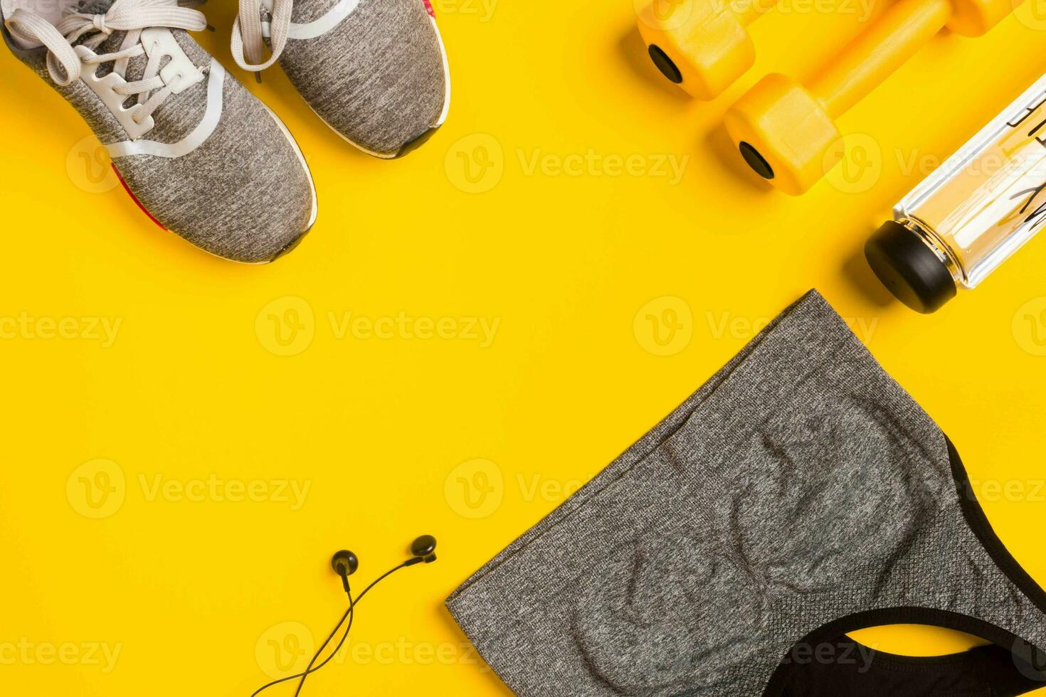 Fitness accessories on a yellow background. Sneakers, bottle of water, headphones and sport top. photo