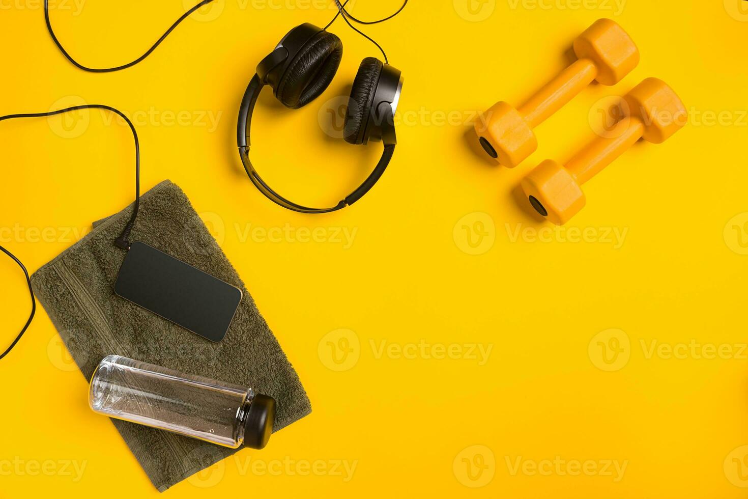 Fitness accessories on a yellow background. Dumbbells, bottle of water, towel and headphones. photo