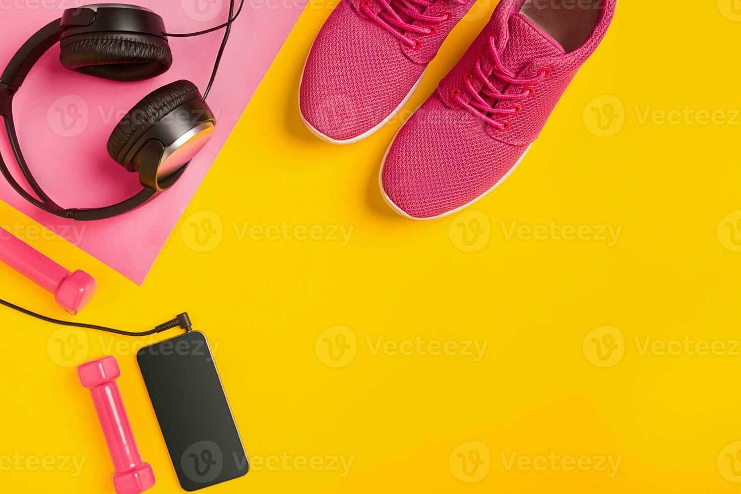 Fitness accessories on a yellow background. Sneakers, bottle of water, earphones and dumbbells. photo