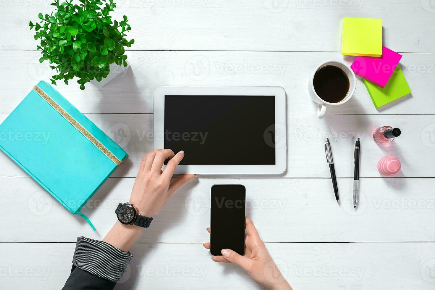 Close up of woman's hands with long fingers holding tablet. Smartphone and notebook lie on table. Top view. photo