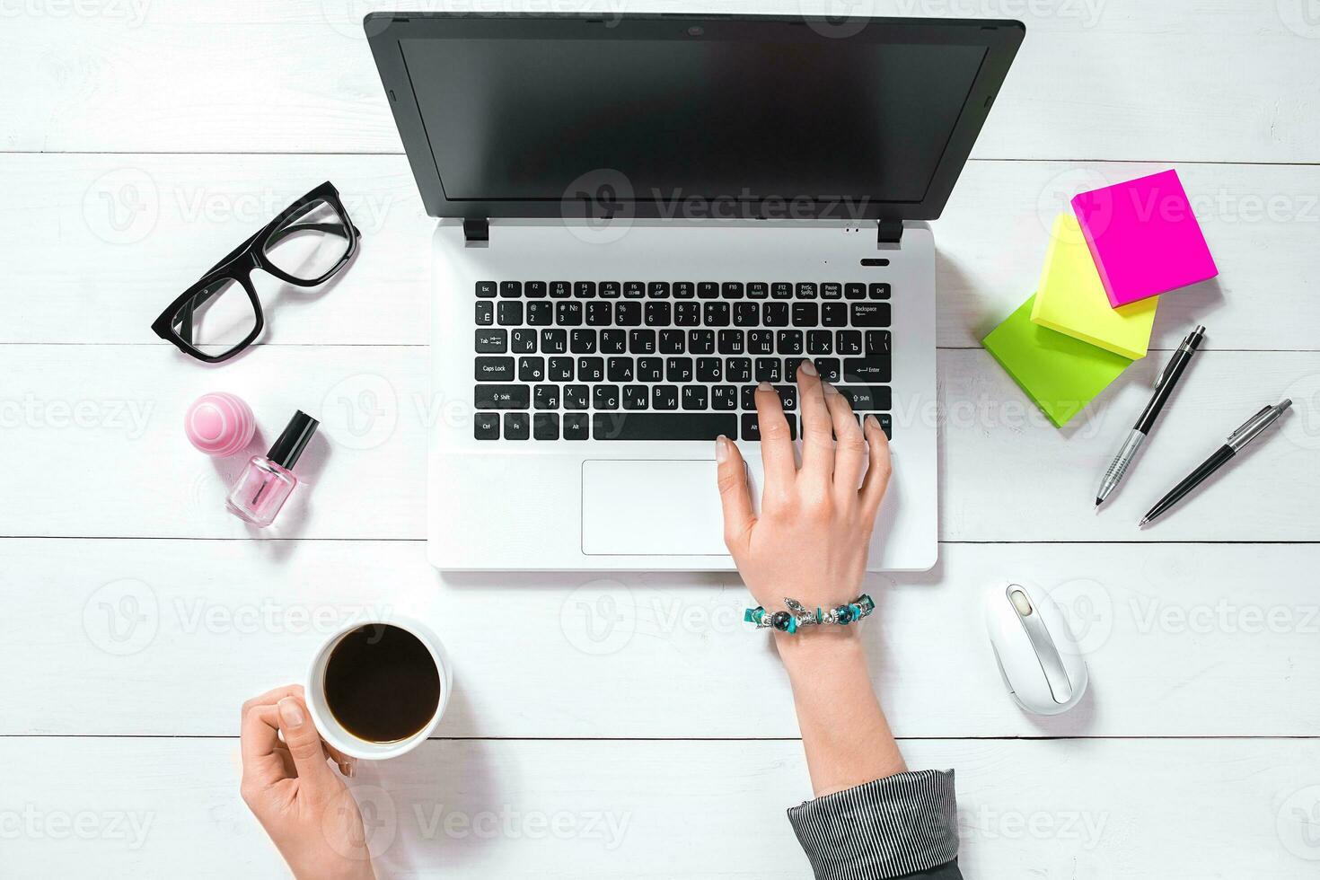 Top view of woman's hands typing on laptop keypad placed on white office desktop with coffee cup. photo