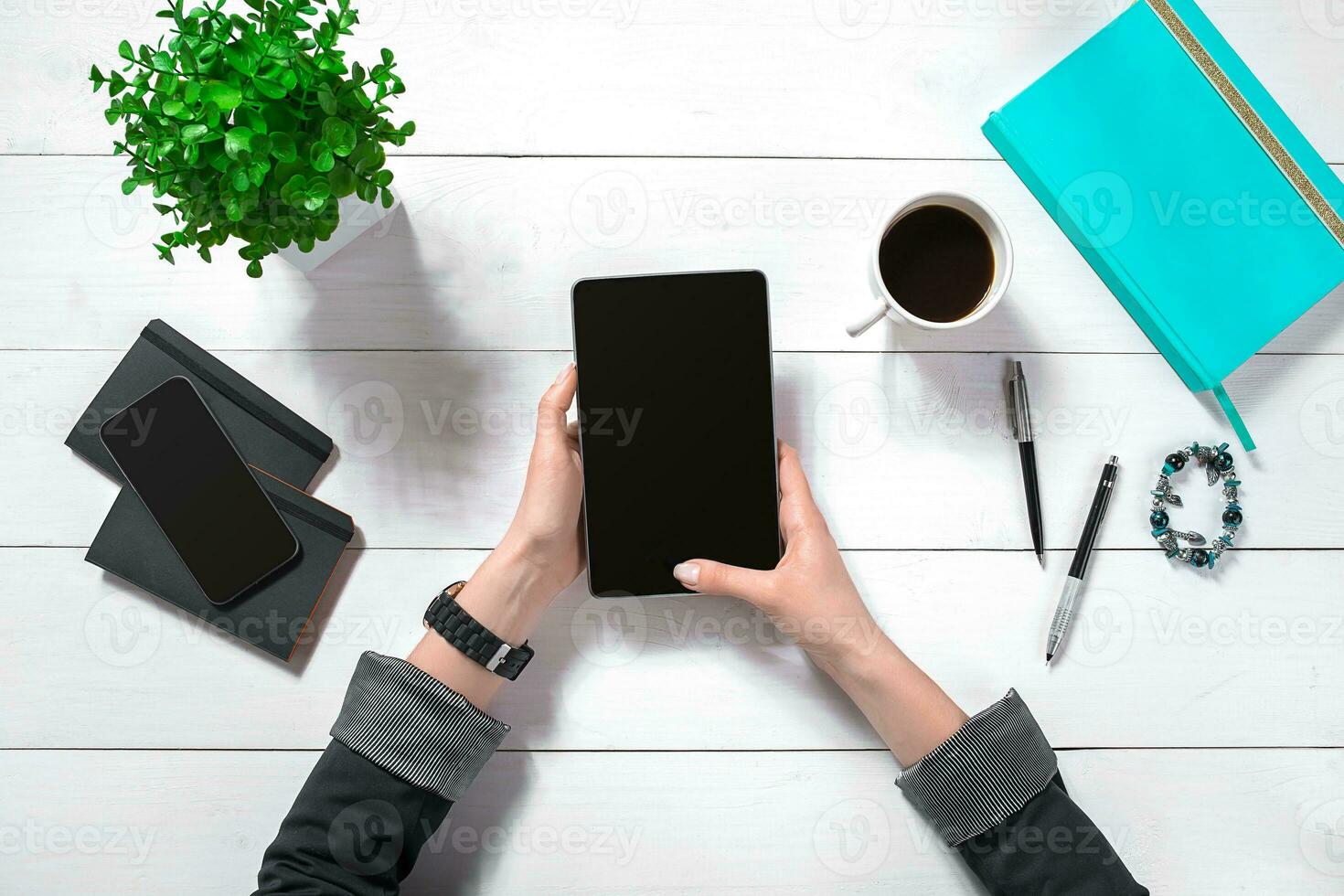 Close up of woman's hands with long fingers holding tablet. Smartphone and notebook lie on table. Top view. photo