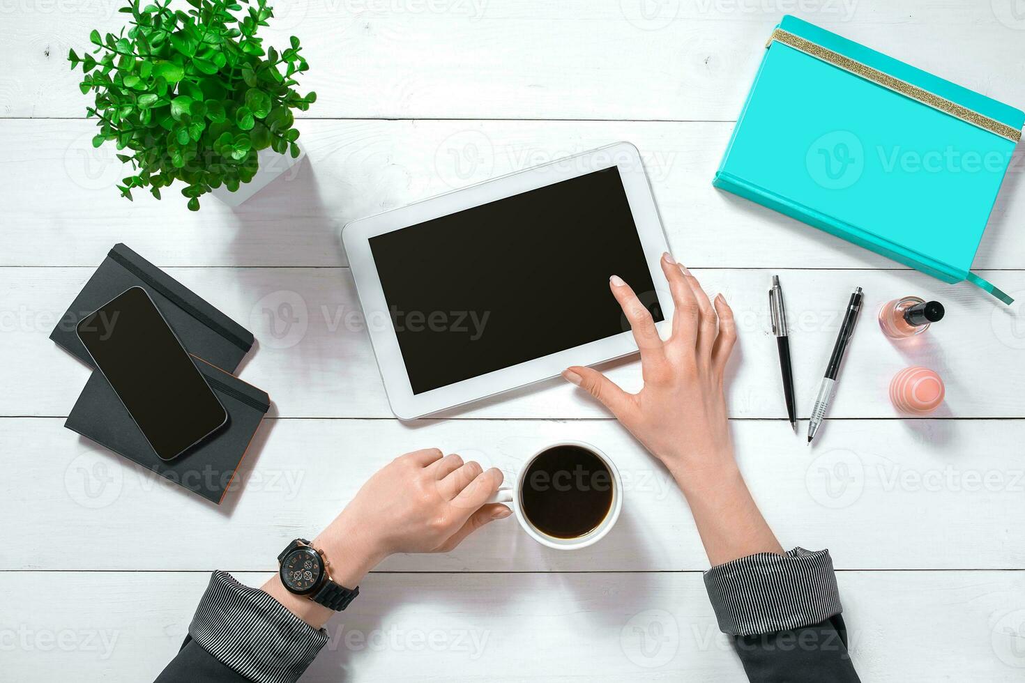 Close up of woman's hands with long fingers holding tablet. Smartphone and notebook lie on table. Top view. photo