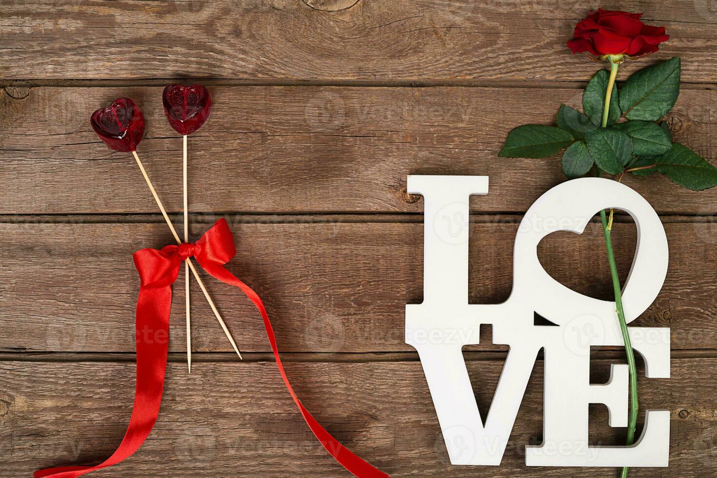 Red rose and candy over wooden background photo