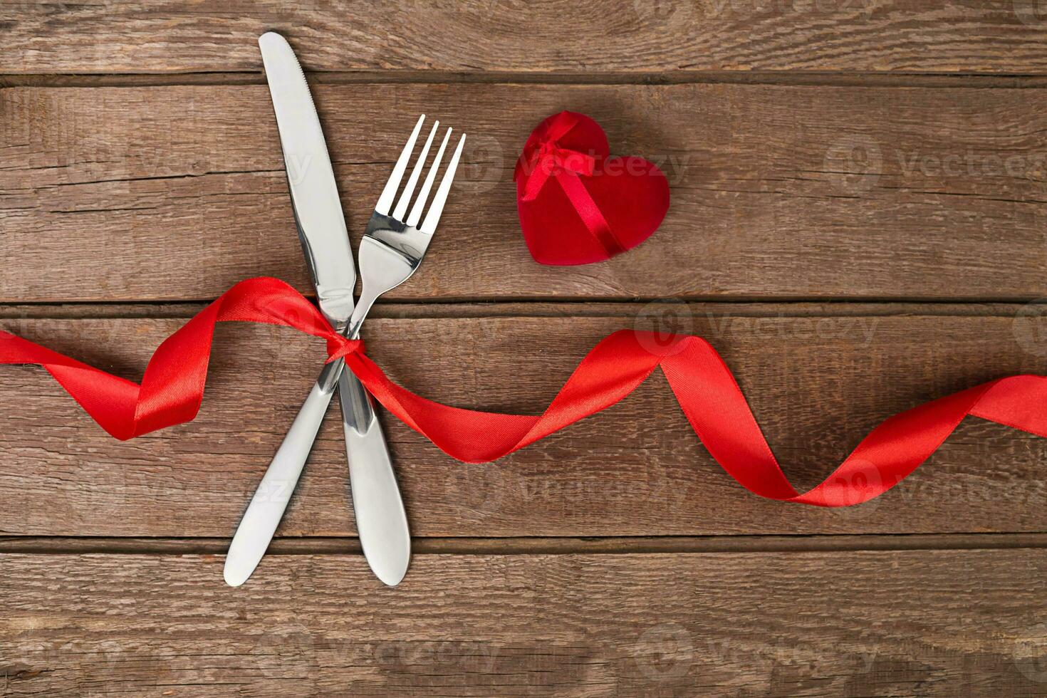 Valentine's Day dinner table setting with red ribbon, knife and fork ring over oak background. photo