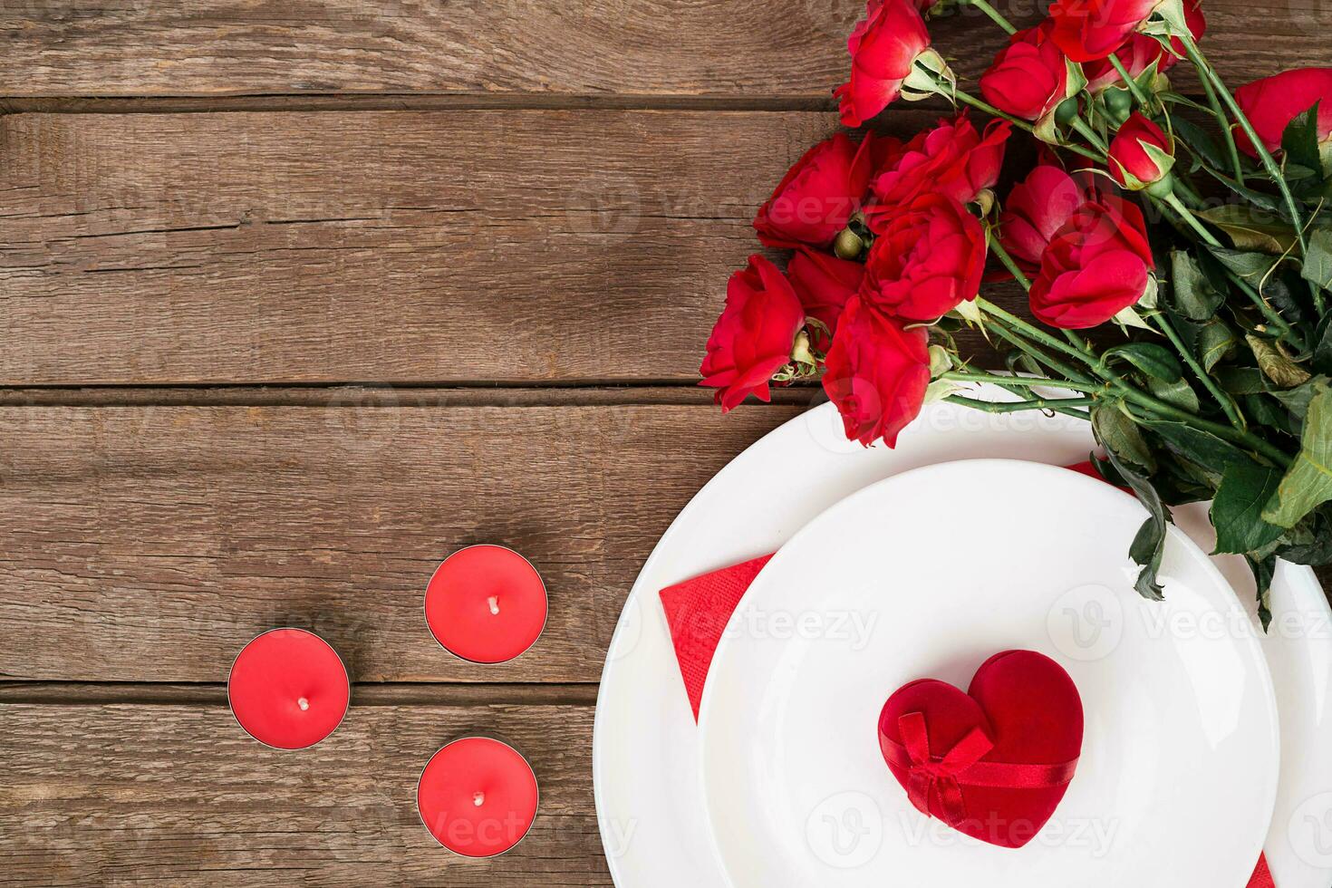 Valentine's Day dinner table setting with red ribbon, roses, knife and fork ring over oak background. photo