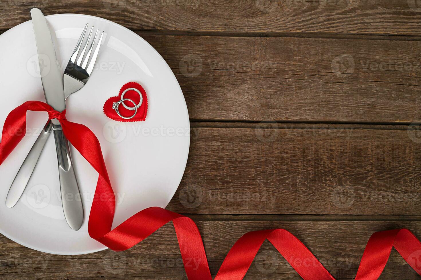 Valentines day table setting with plate, fork, knife, red heart, ring and ribbon. background photo