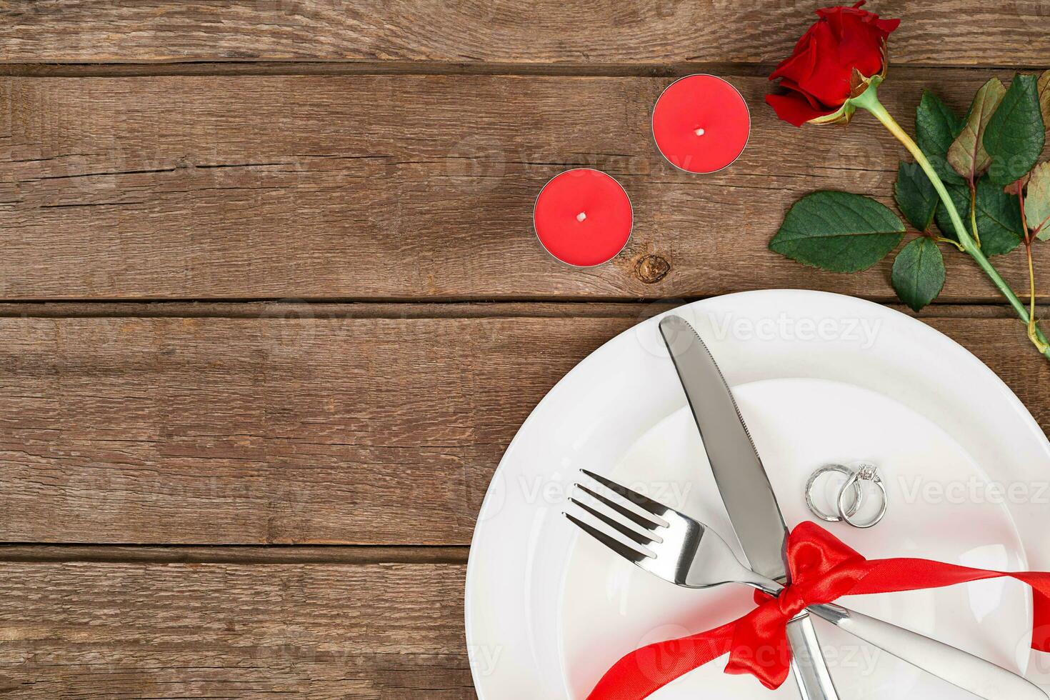 Valentine's Day dinner table setting with red ribbon, rose, knife and fork ring over oak background. photo