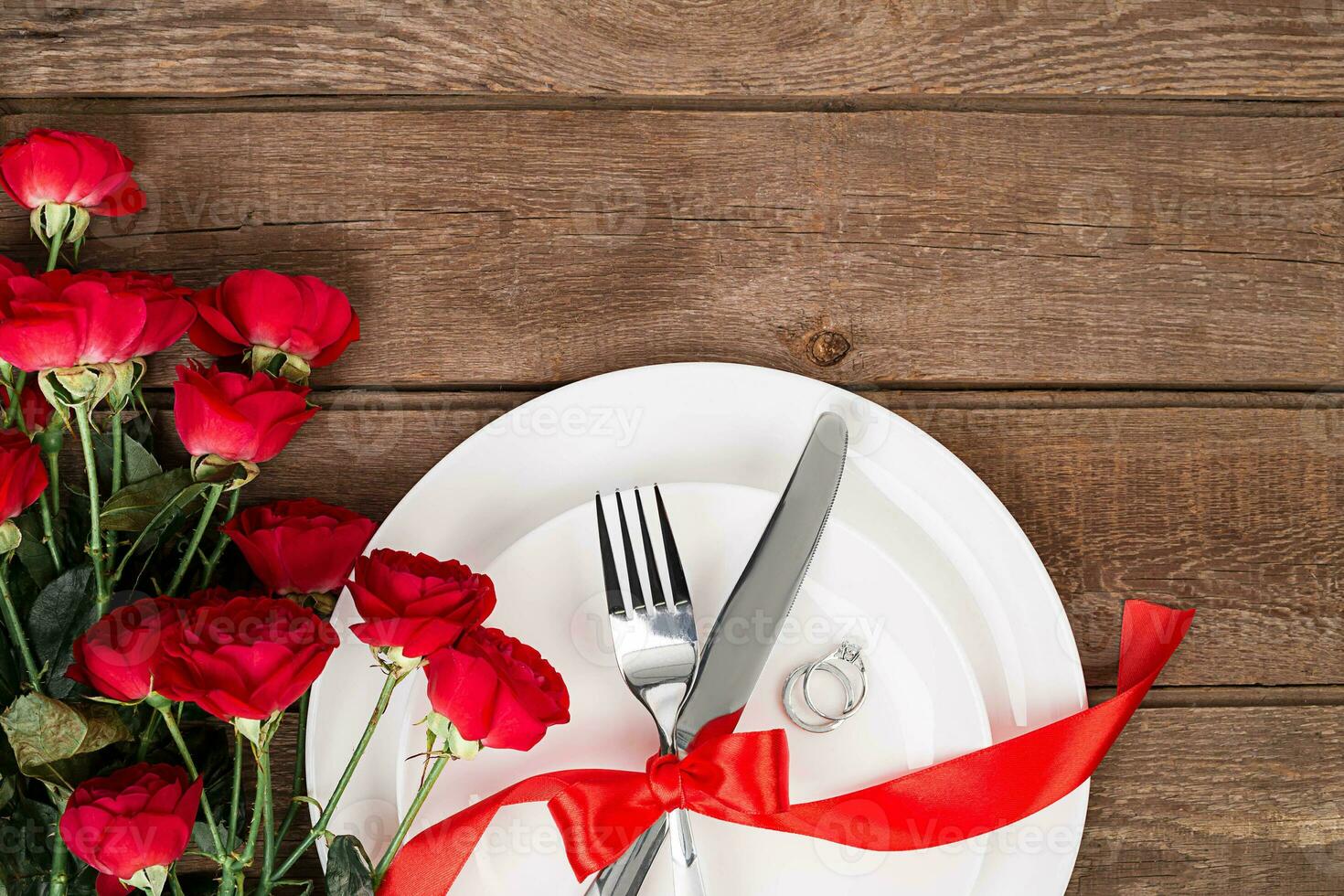 San Valentín día cena mesa ajuste con rojo cinta, rosas, cuchillo y tenedor anillo terminado roble antecedentes. foto