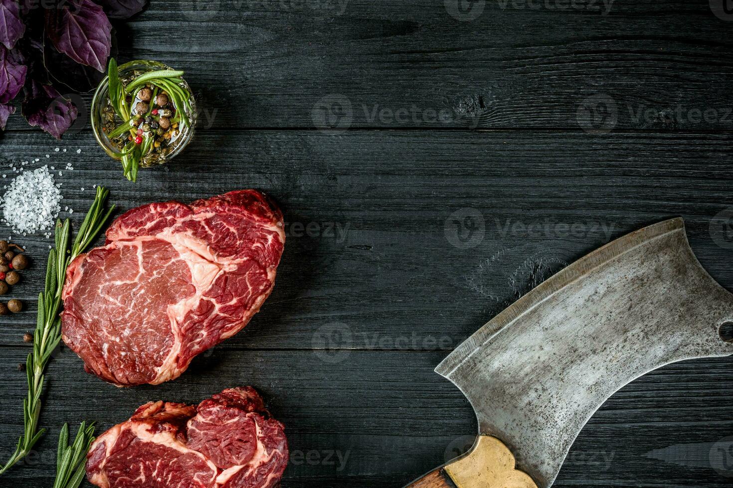 Fresh raw beef with basil and a sprig of rosemary with ax for meat on black wooden background. Top view photo