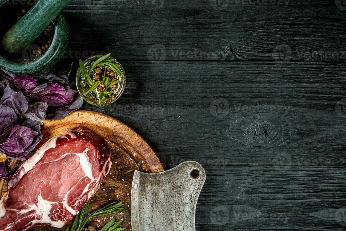 Fresh raw beef with basil and a sprig of rosemary with ax for meat on black wooden background. Top view photo