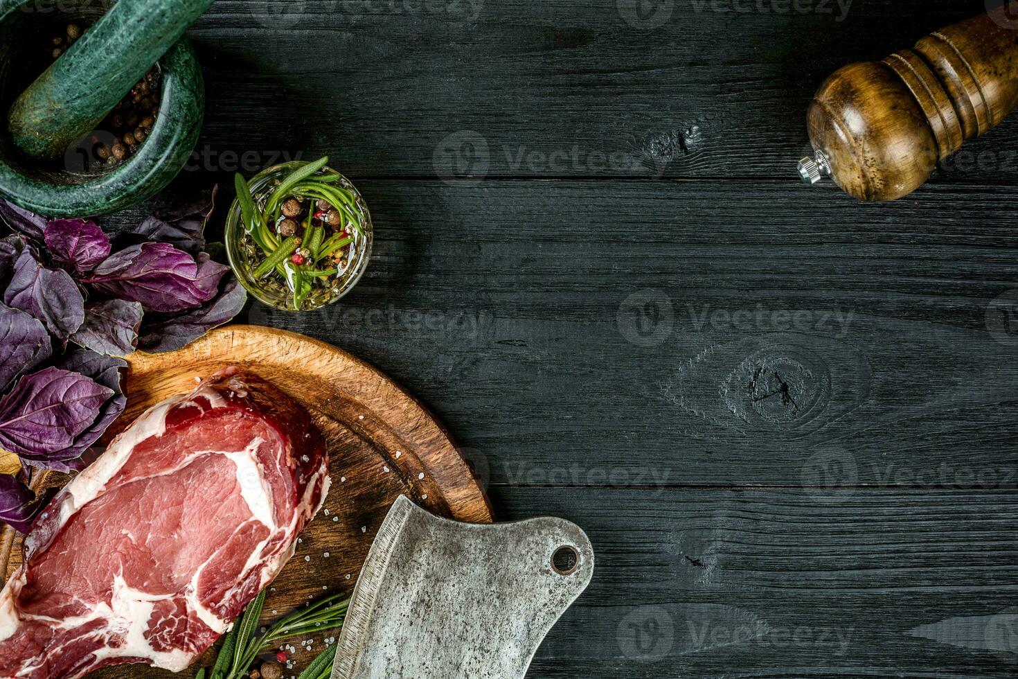 Fresh raw beef with basil and a sprig of rosemary with ax for meat on black wooden background. Top view photo