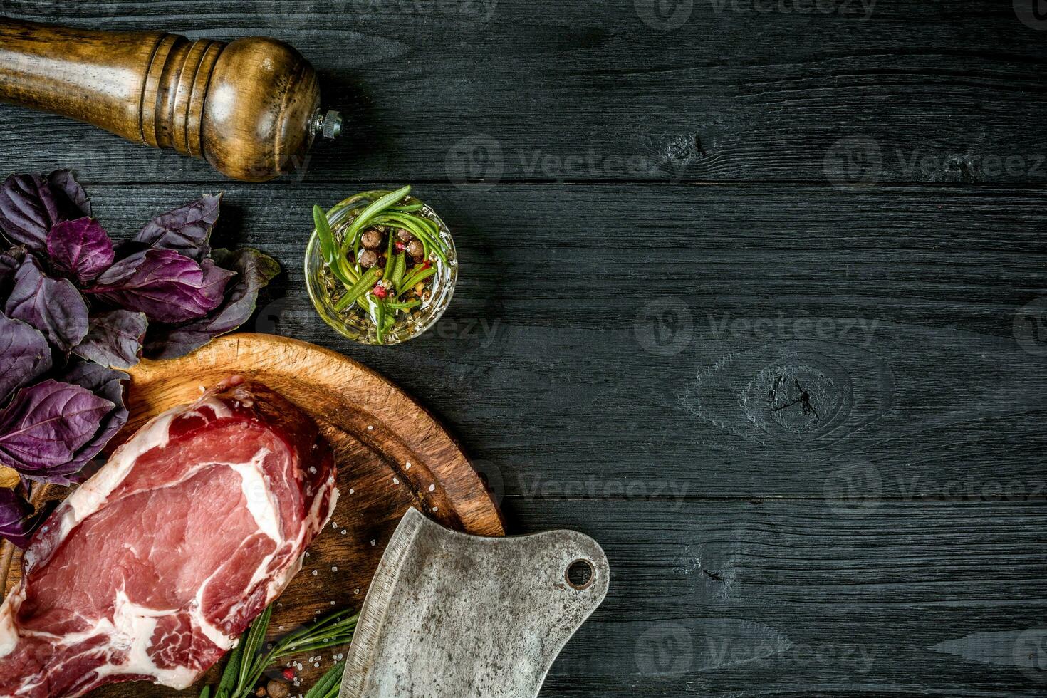 Fresh raw beef with basil and a sprig of rosemary with ax for meat on black wooden background. Top view photo