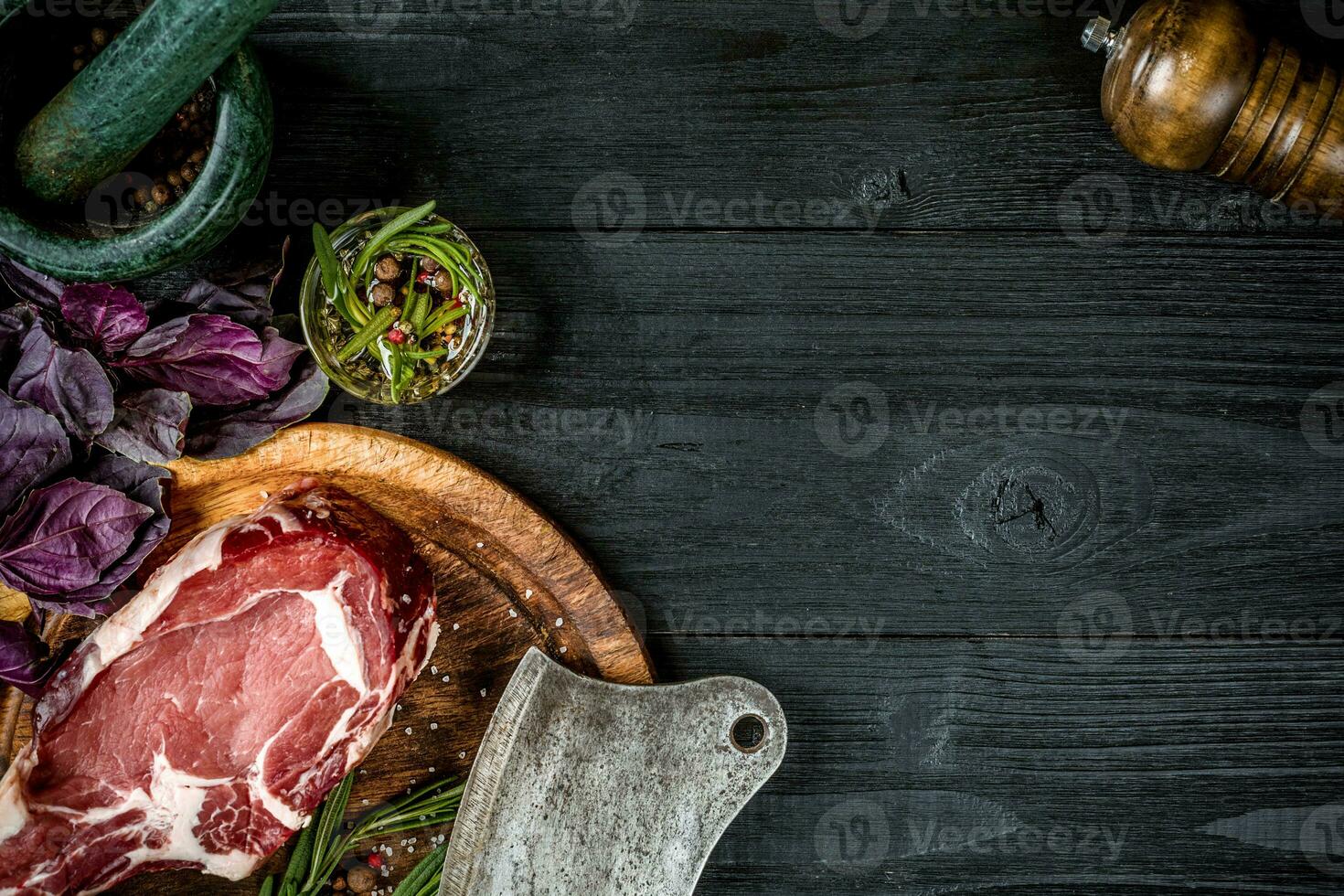 Fresh raw beef with basil and a sprig of rosemary with ax for meat on black wooden background. Top view photo
