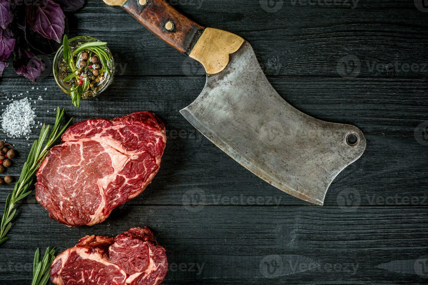 Fresh raw beef with basil and a sprig of rosemary with ax for meat on black wooden background. Top view photo