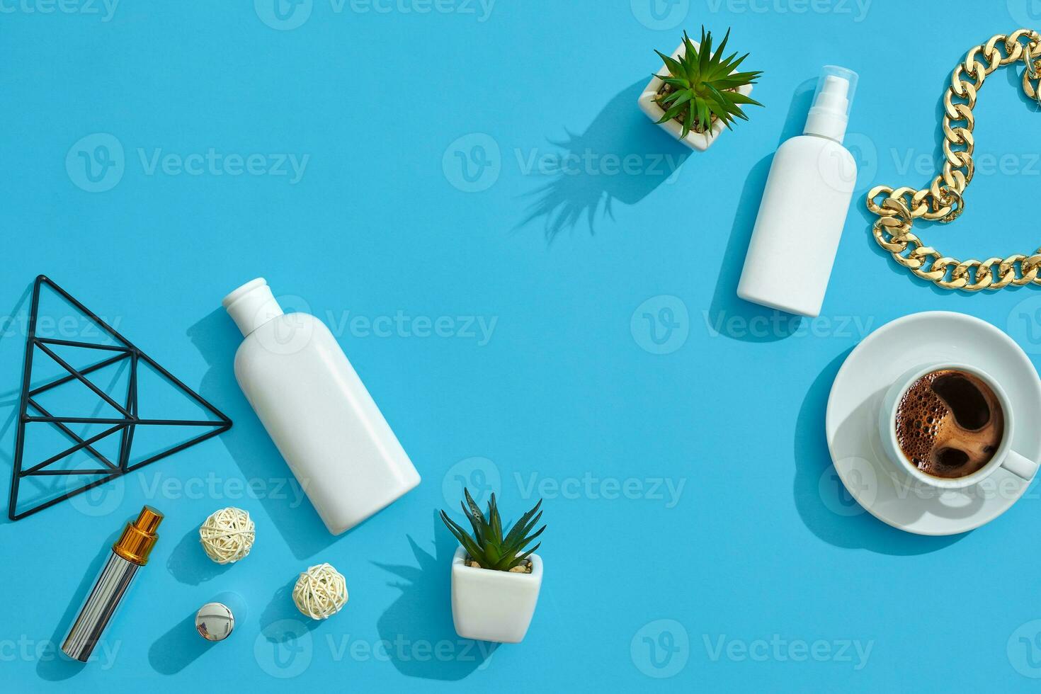 White flask and pump bottle with no label, cup of coffee, chain, figurine of triangle, perfume container on blue background. Close up, copy space photo