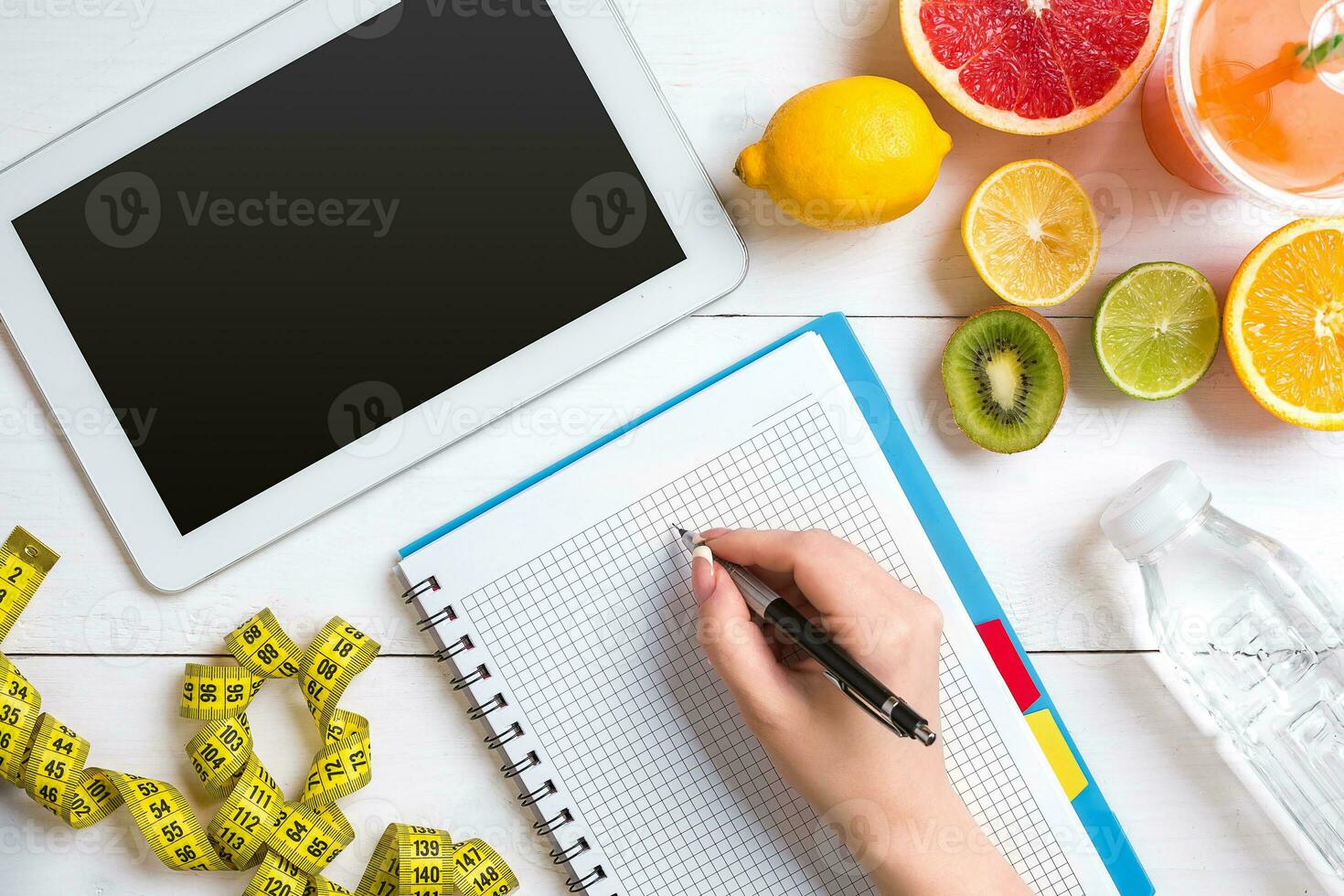 Fresh juice in glass from citrus fruits - lemon, grapefruit, orange, notebook with pencil on white wooden background photo