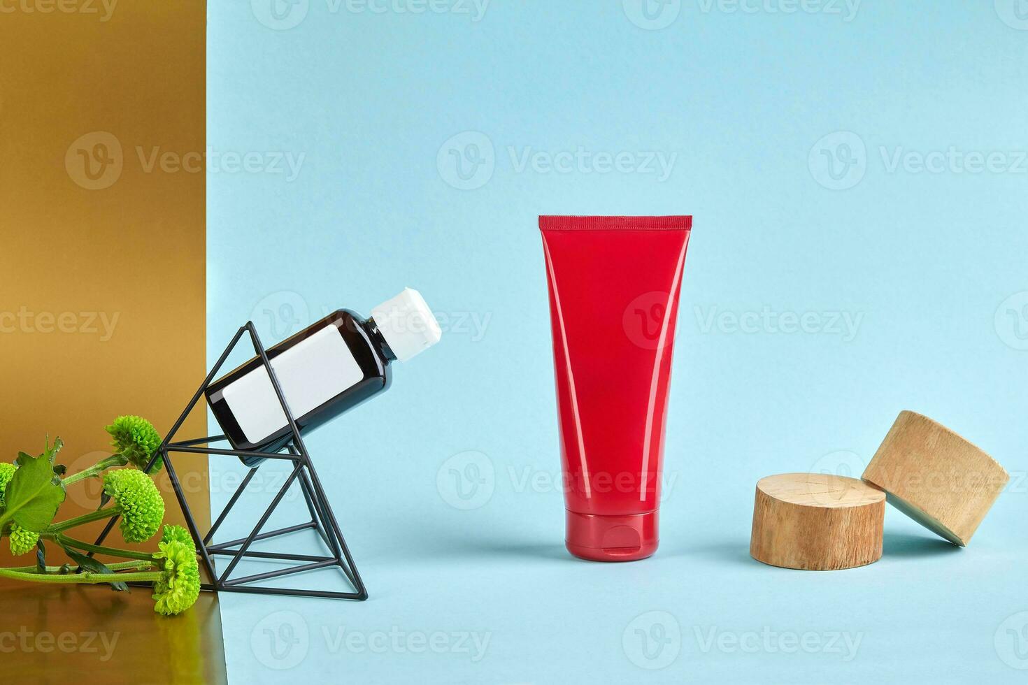 Red cosmetic tube with no logo, wooden stands, plastic bottle on figurine of triangle and green flowers, colorful background. Close up, copy space photo