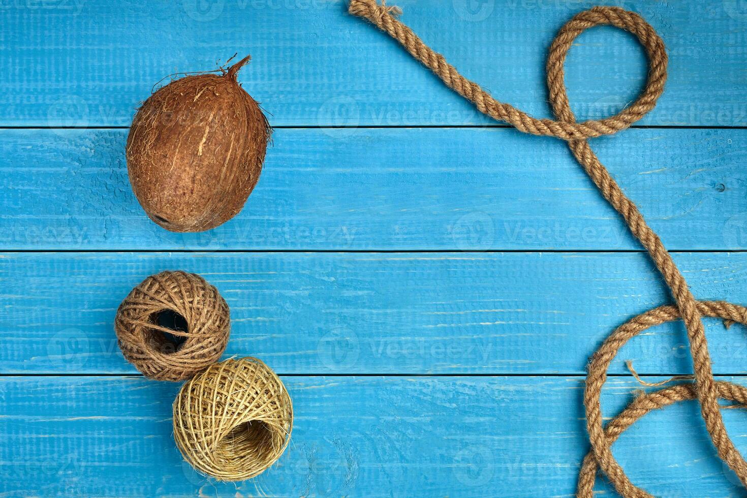 Ripe coconut, two skeins of jute twine or thread and a rope on blue wooden background or desktop. Close up, copy space photo