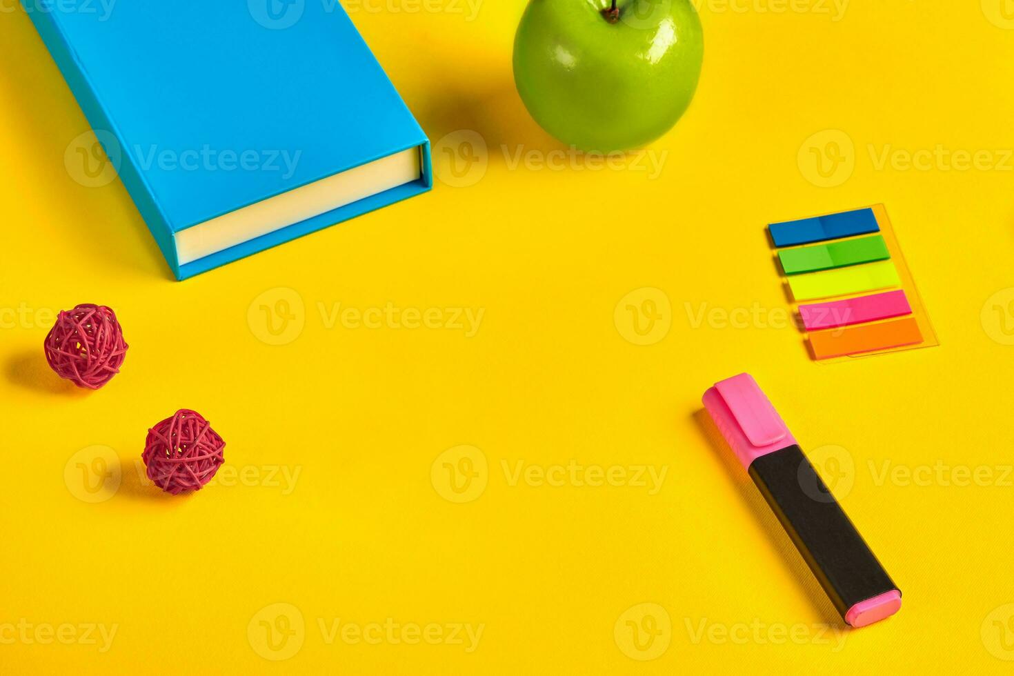 Blue box or notebook, green apple, pink marker, colorful sticky notes and two decorative rattan balls on yellow background. Close up, copy space photo