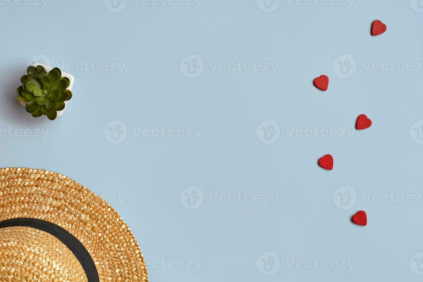 Straw hat, green succulent in white pot and wooden red hearts over blue background. Close up, copy space photo