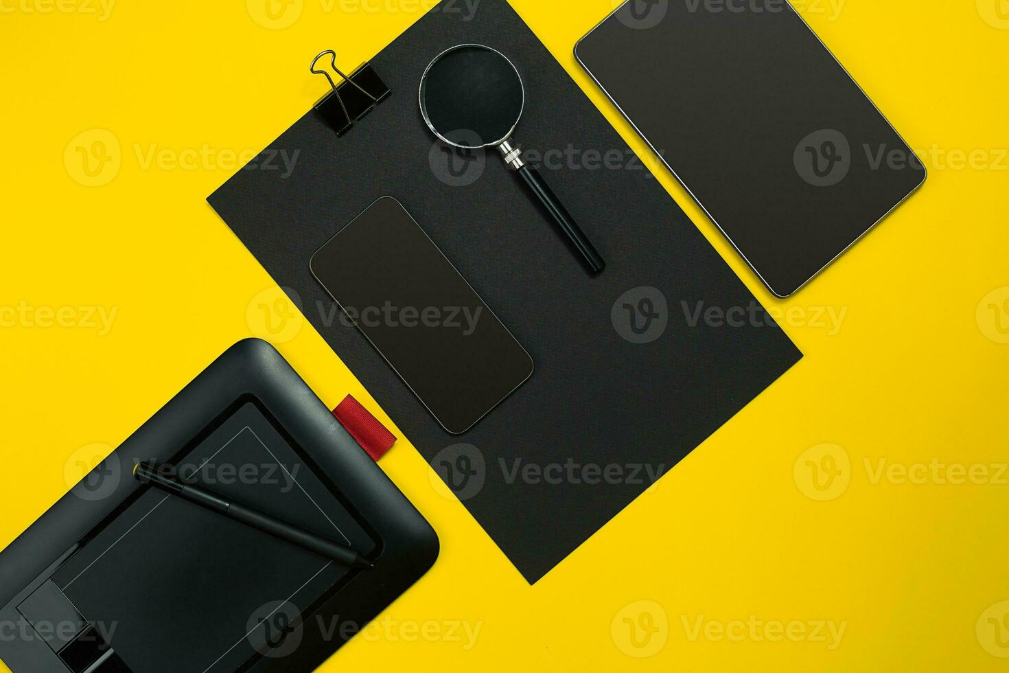 Flat lay display of business office gadgets with notepad, cup, pen, develop, glasses and etc. Top view. Black office objects on a yellow background photo