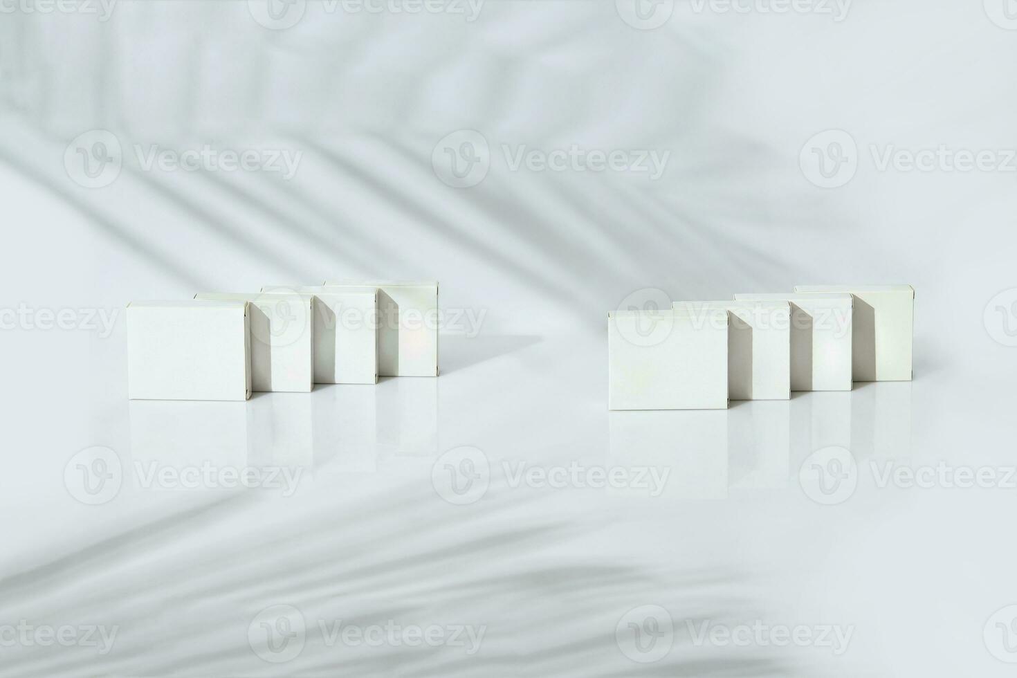 Eight small cardboard boxes with no logo isolated on white studio background. Palm tree twig shadow. Copy space, branding area photo