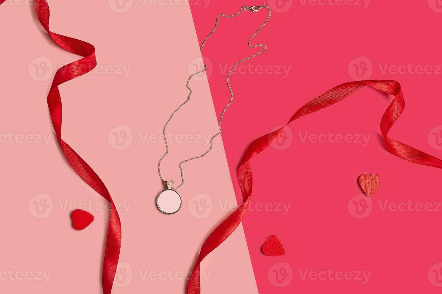 Blank pendant or medallion on a chain next to red ribbons and cut out cardboard hearts against colorful studio background. Close up, copy space photo