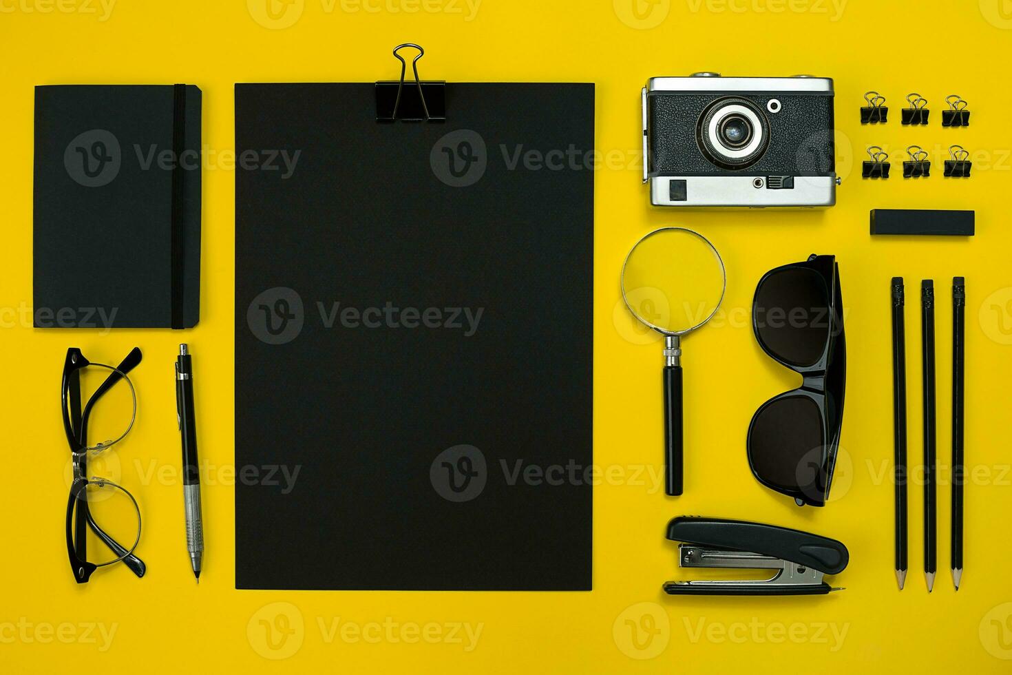 Flat lay display of business office gadgets with notepad, vintage camera, pen, develop, glasses and etc. Top view. Black office objects on a yellow background photo