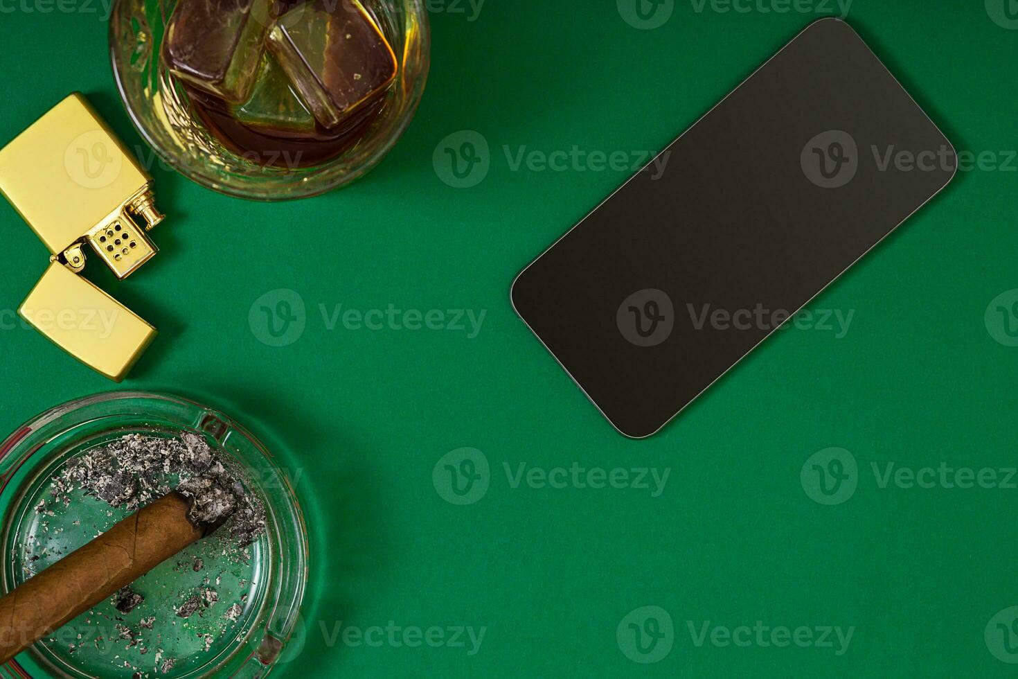 top of view of cigar in an ashtray near whiskey glass on green poker table photo