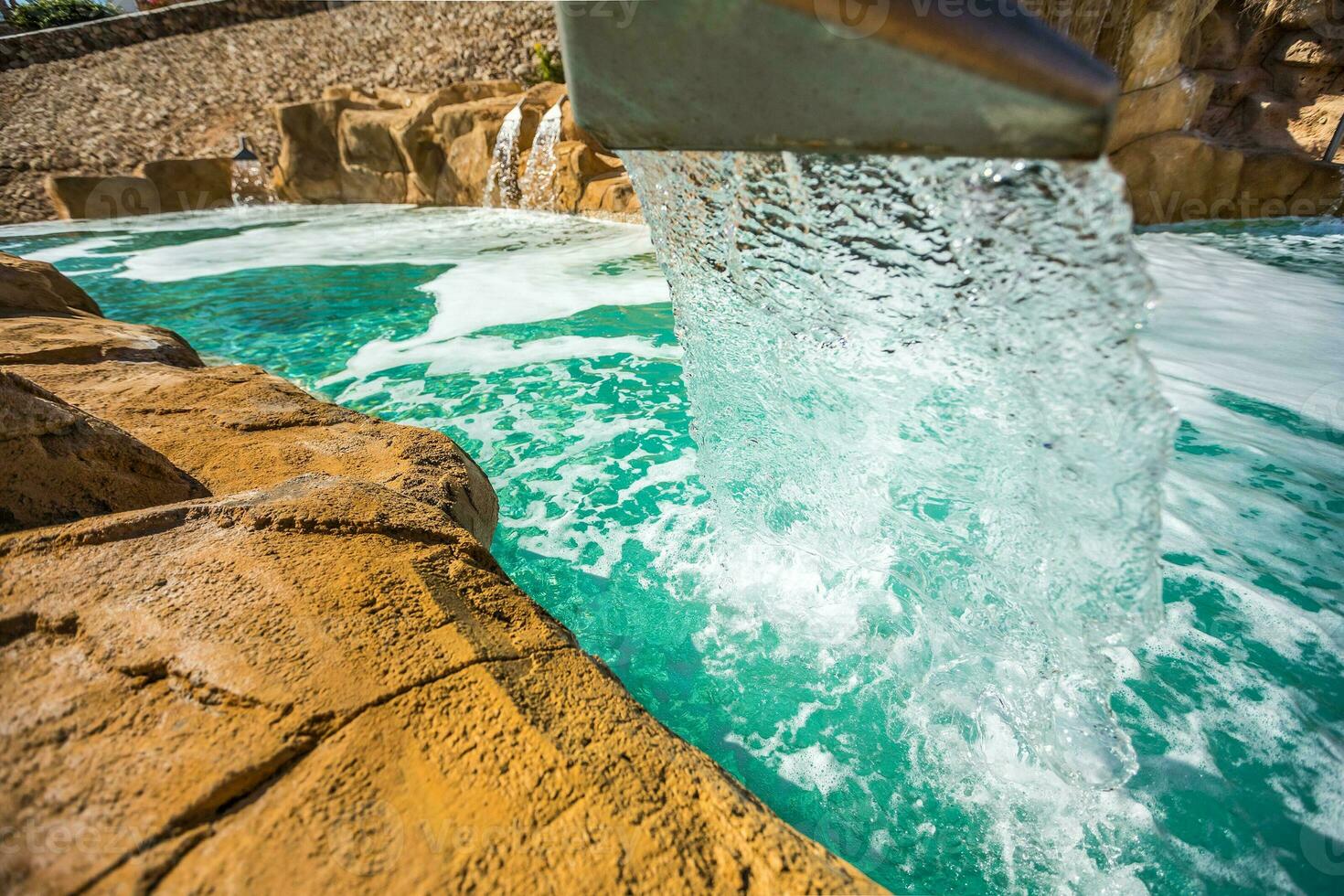 Stream water out of artificial waterfall in outdoor pool photo