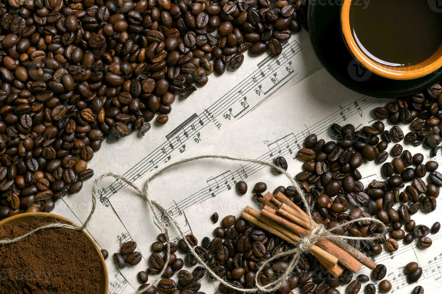 Coffee beans, ground coffee and cup of brewed coffee on sheet music background, view from above with space for text photo