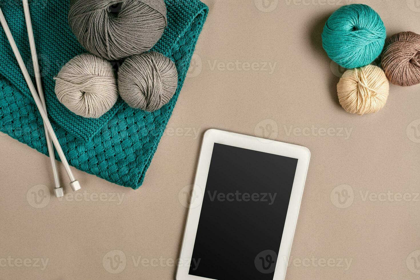 Grey and turquoise knitting wool, knitting needles and a tablet with a black screen on beige background. Top view. Copy space photo