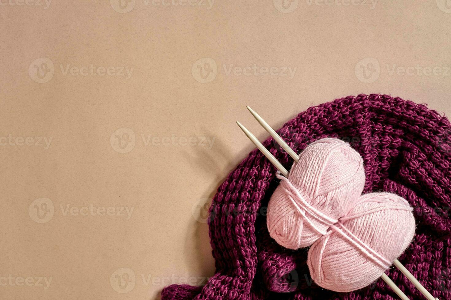 Two pink knitting yarn balls, knitting needles and and purple knitted plaid top view photo