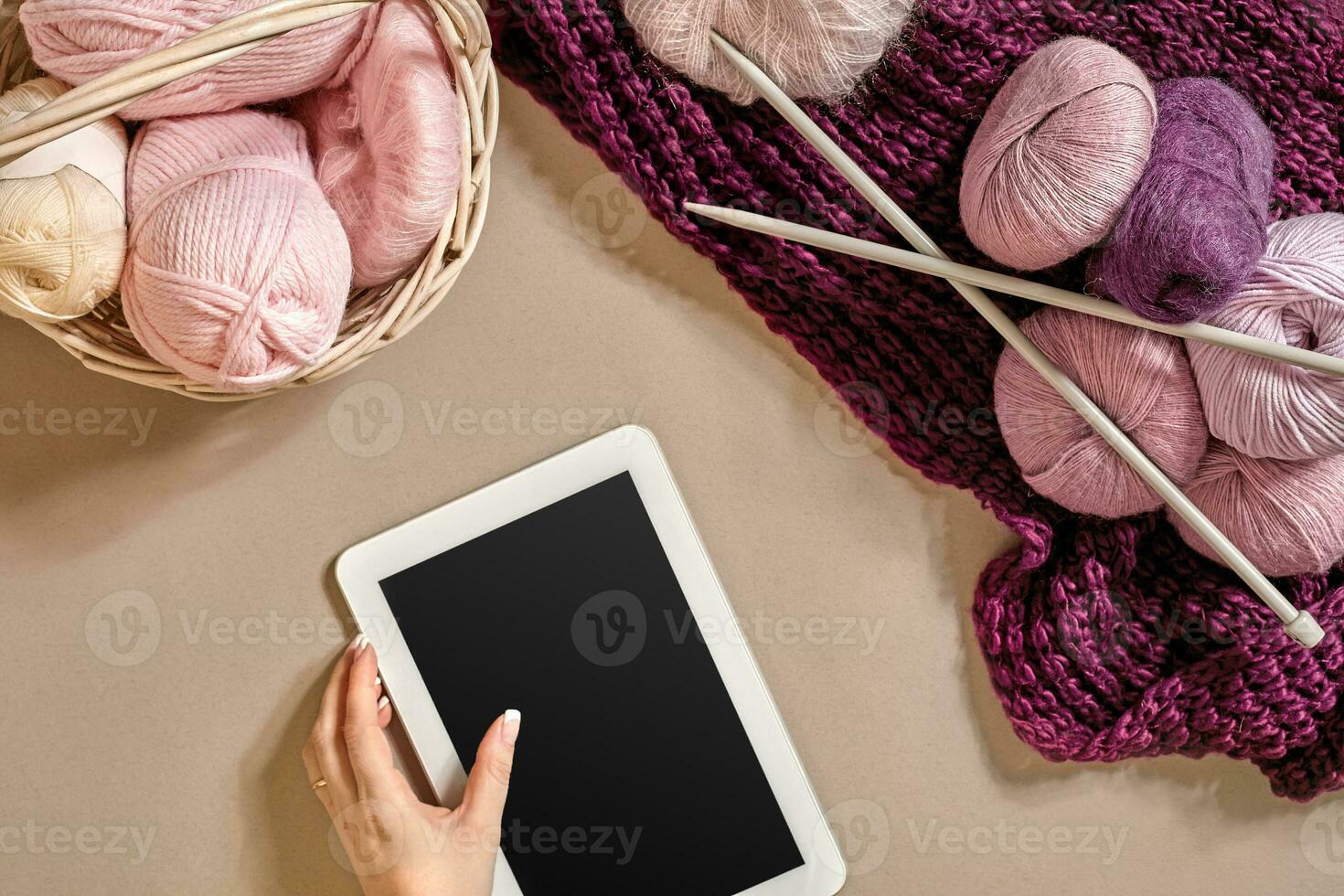Pink and purple balls of wool threads with knitting needles lying in basket on beige background. Mock up background for your craft knitting photo