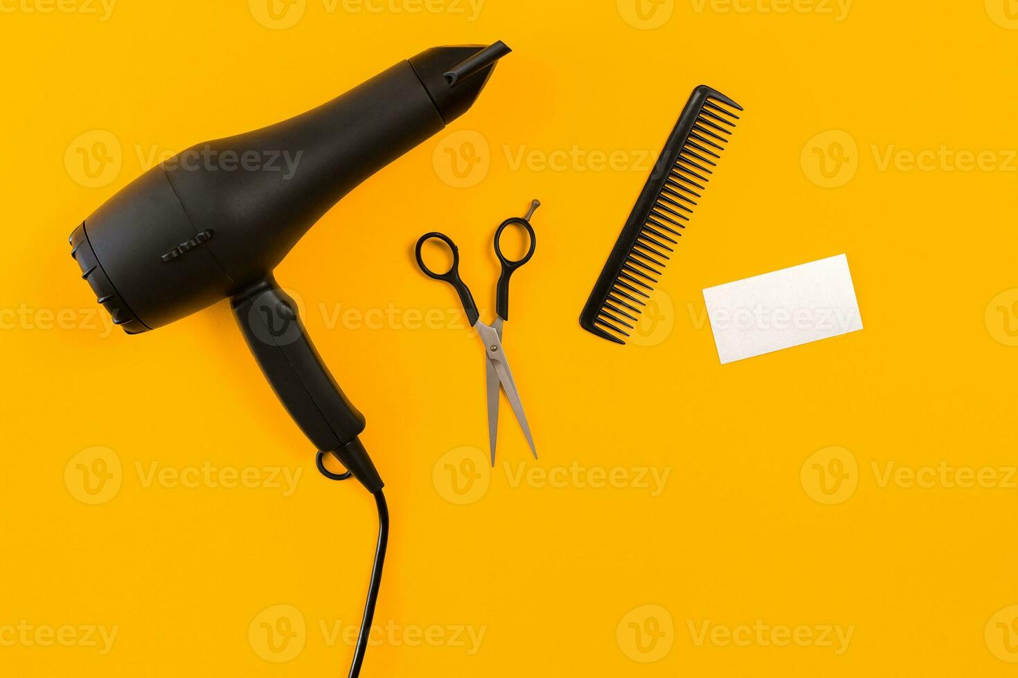 Black hair dryer, comb and scissors on yellow paper background. Top view photo