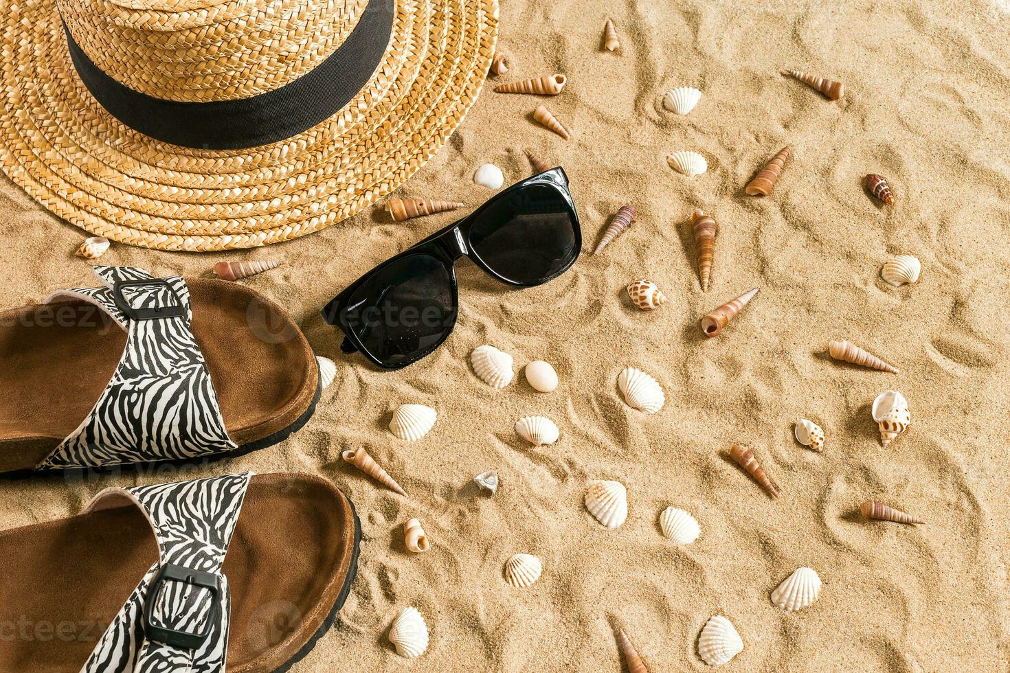 Summer beachwear, flip flops, hat, sunglasses and seashells on sand beach. photo