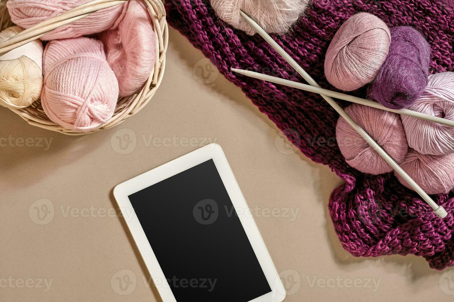 Pink and purple balls of wool threads with knitting needles lying in basket on beige background. Mock up background for your craft knitting photo