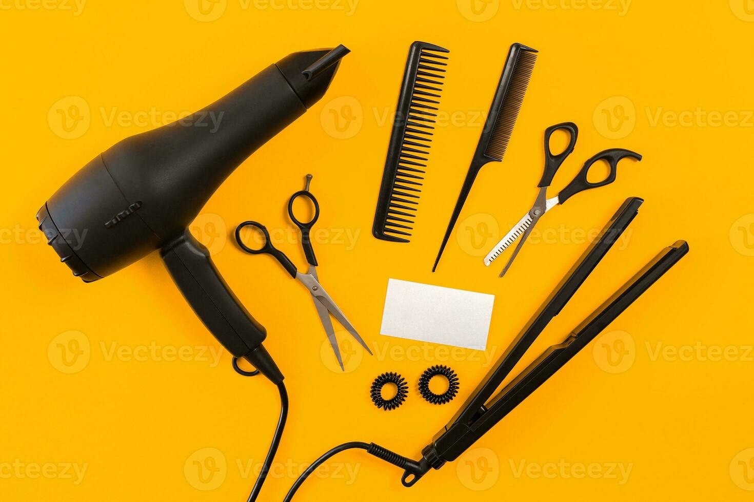 Black hair dryer, comb and scissors on yellow paper background. Top view photo