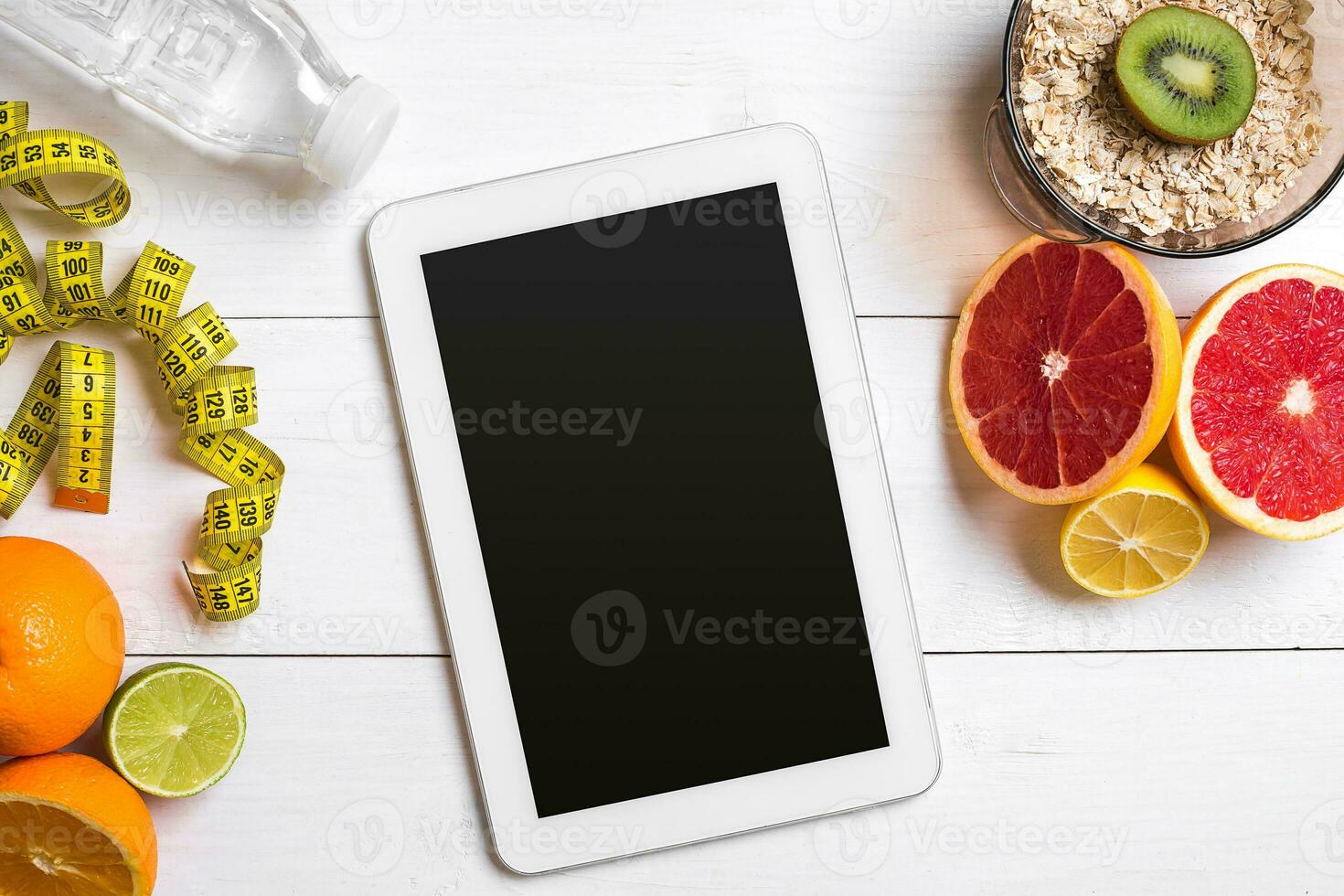 Healthy breakfast with oatmeal, fresh fruits and bottle of water with tablet on rustic wooden table. photo