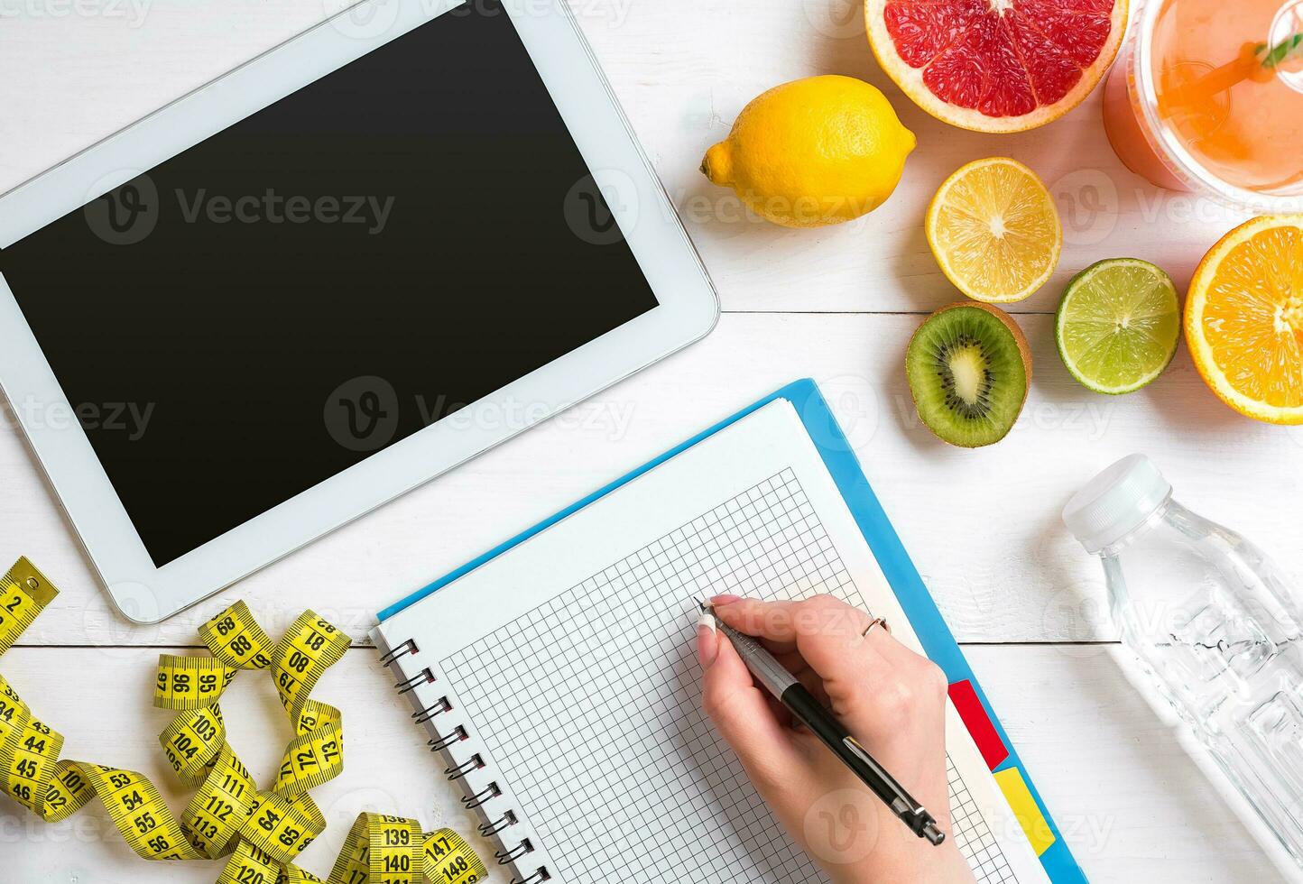 Fresh juice in glass from citrus fruits - lemon, grapefruit, orange, notebook with pencil on white wooden background photo