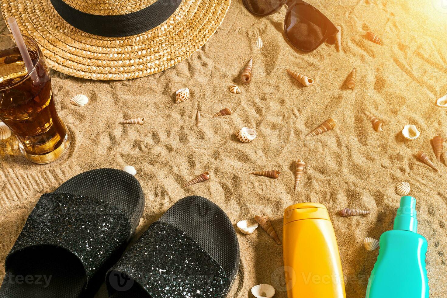 Summer beachwear, flip flops, hat, cold drink in a glass and seashells on sand beach. photo