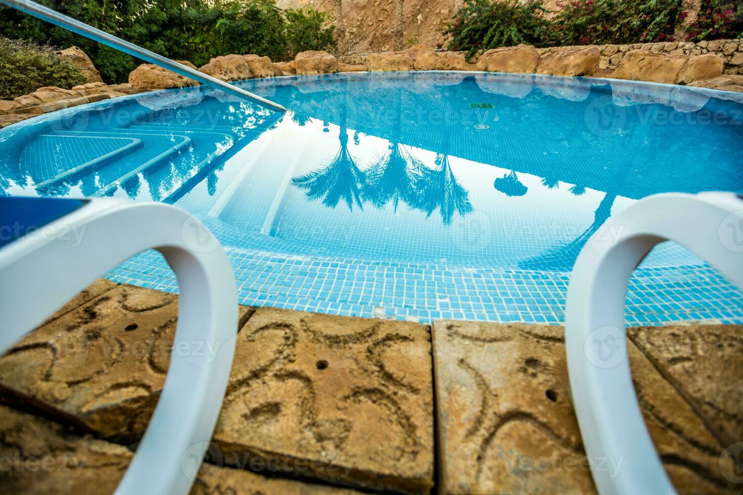Closeup sunloungers and swimming pool with reflected palms in water photo