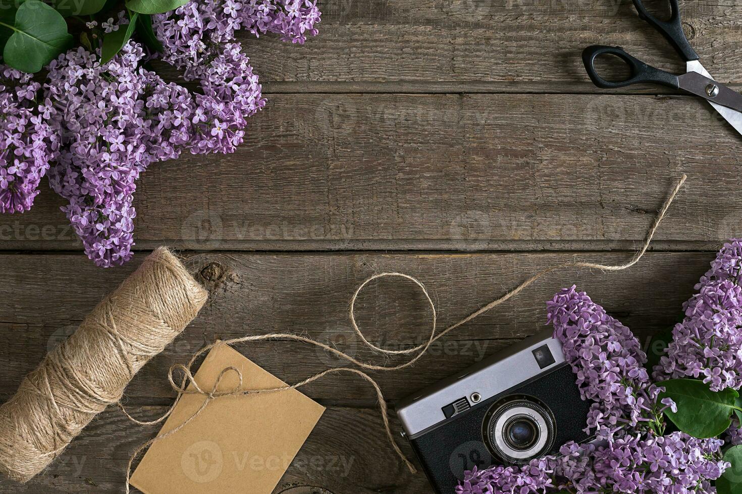 Lilac blossom on rustic wooden background with empty space for greeting message. Scissors, thread reel, small envelope and camera. Top view photo