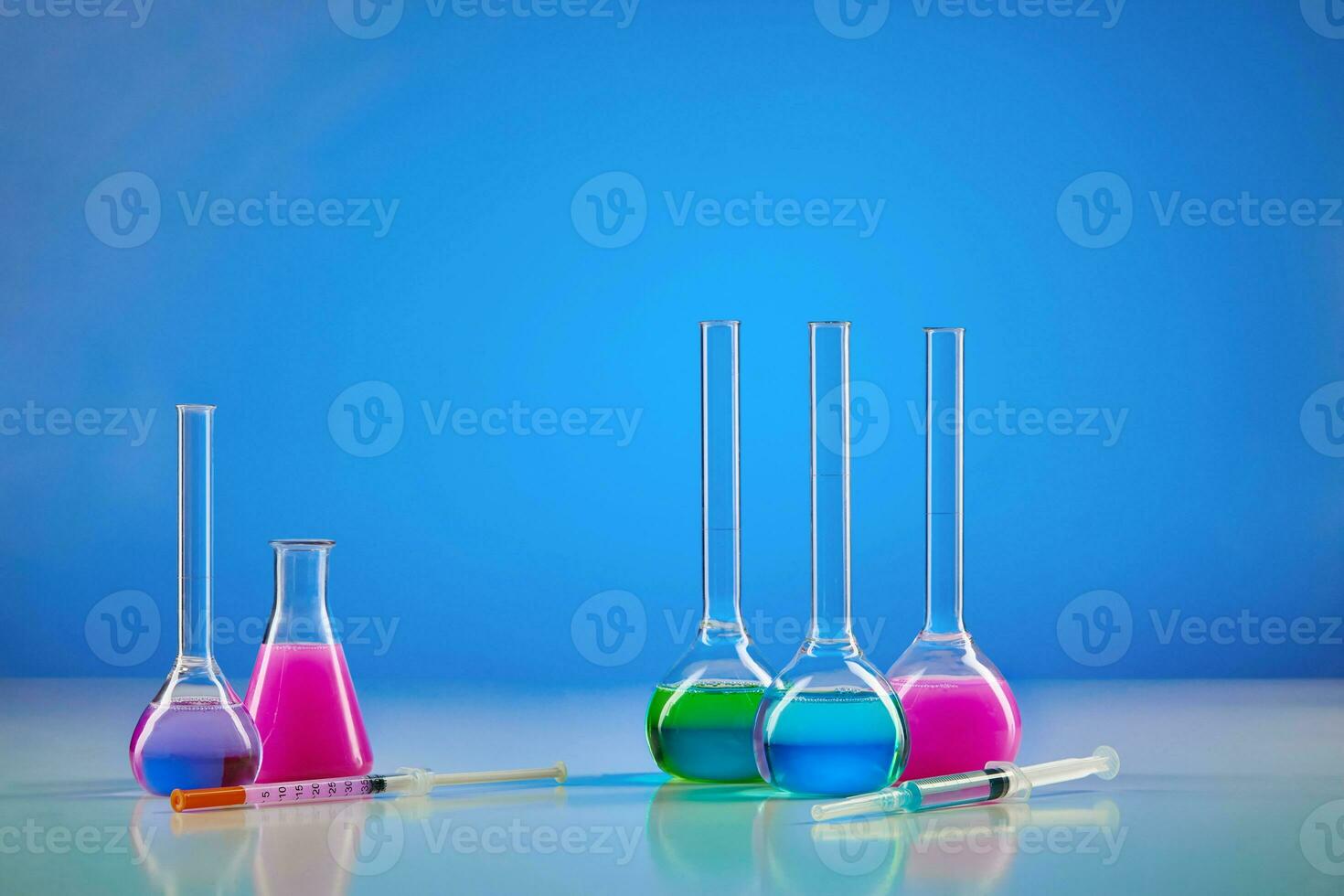 Five medical flasks with colorful chemical reagents. Testing kit and syringe against blue background. Coronavirus. Pandemic COVID-19. Close up photo