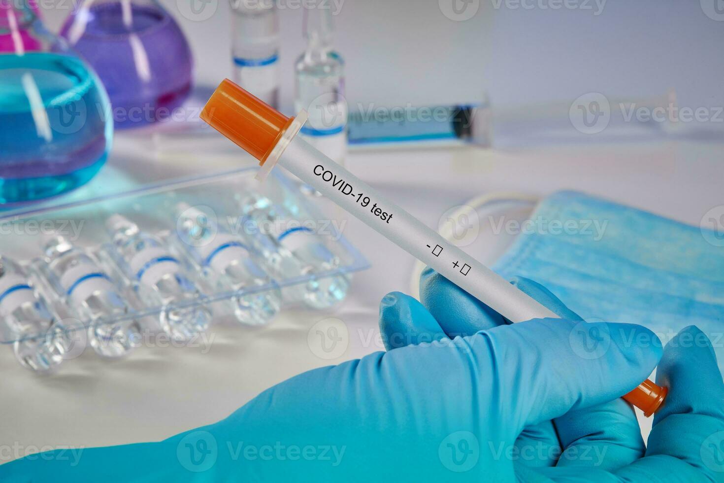 Hand in blue glove holding testing kit. Medical flasks, colorful chemical reagents. Ampoules, mask, syringe isolated on white. Coronavirus. Close up photo