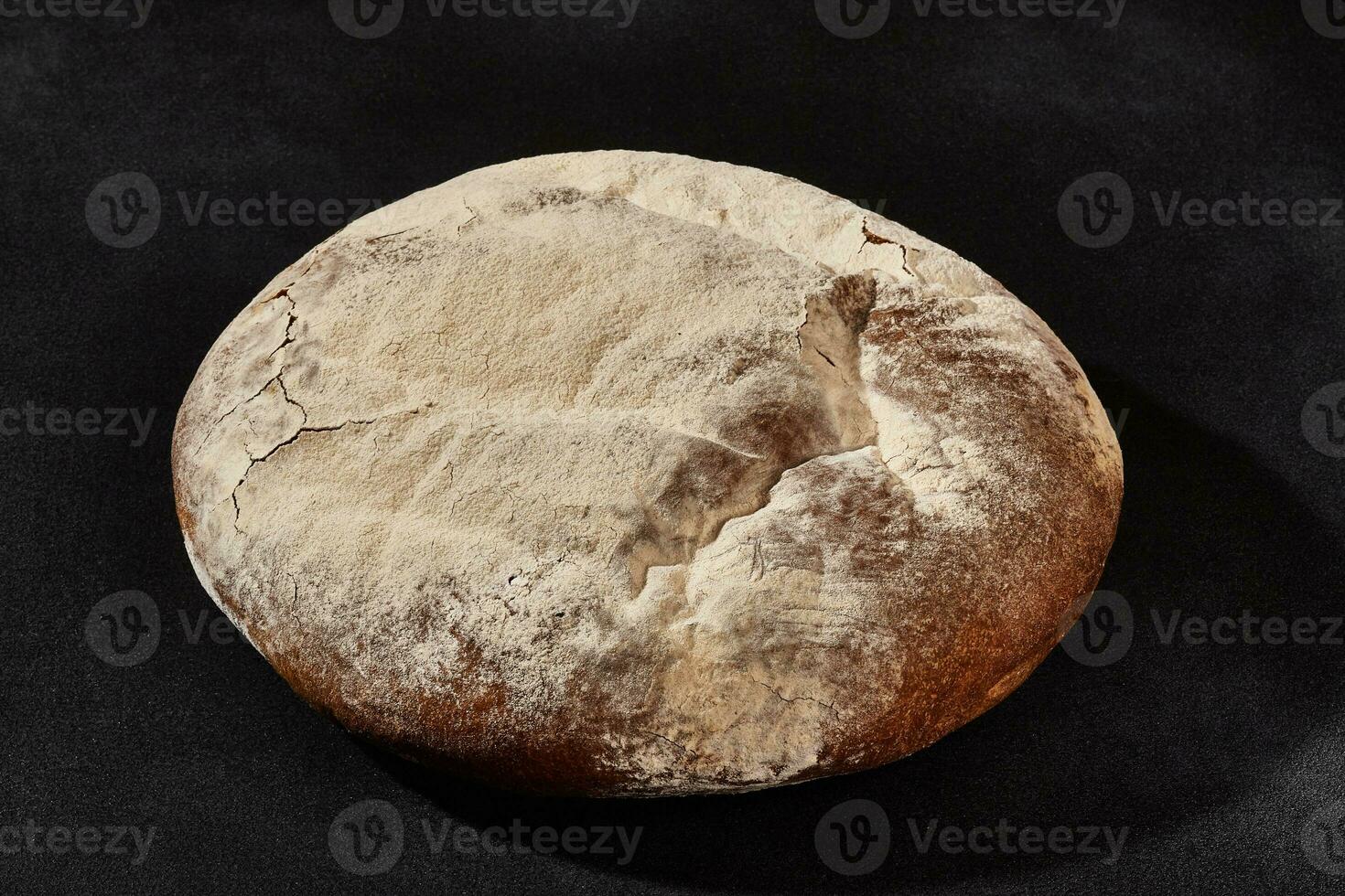 Fresh, delicious baked round bread sprinkled with flour. Black background with copy space. Rural cuisine or bakery. Close-up photo