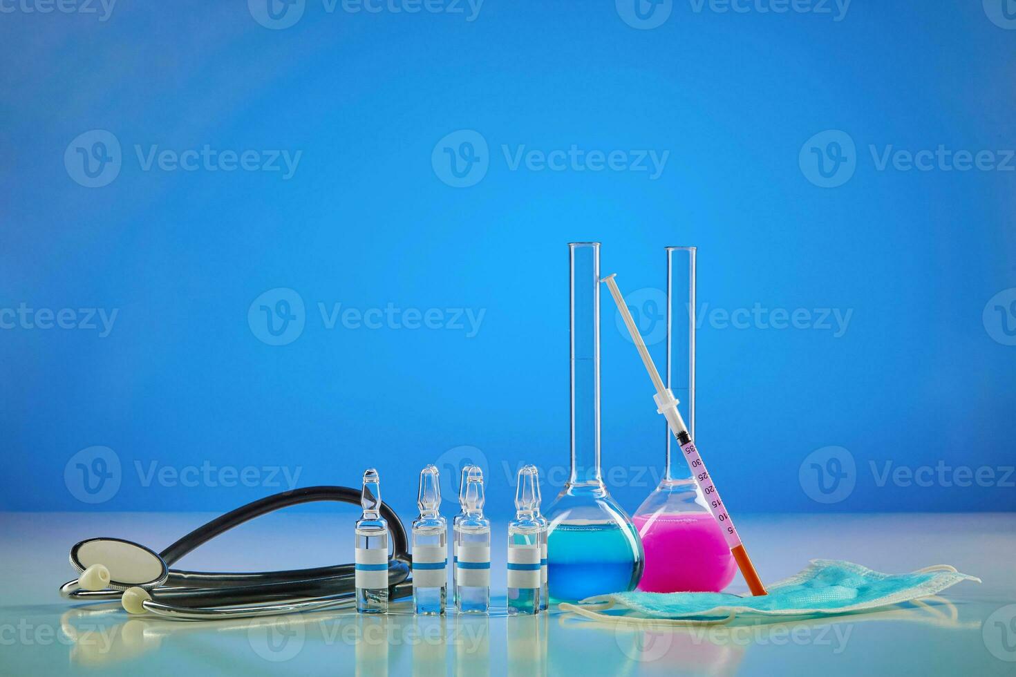 Medical flasks with colorful chemical reagents. Six ampoules with liquid, testing kit, mask and phonendoscope, blue background. Coronavirus , pandemic photo