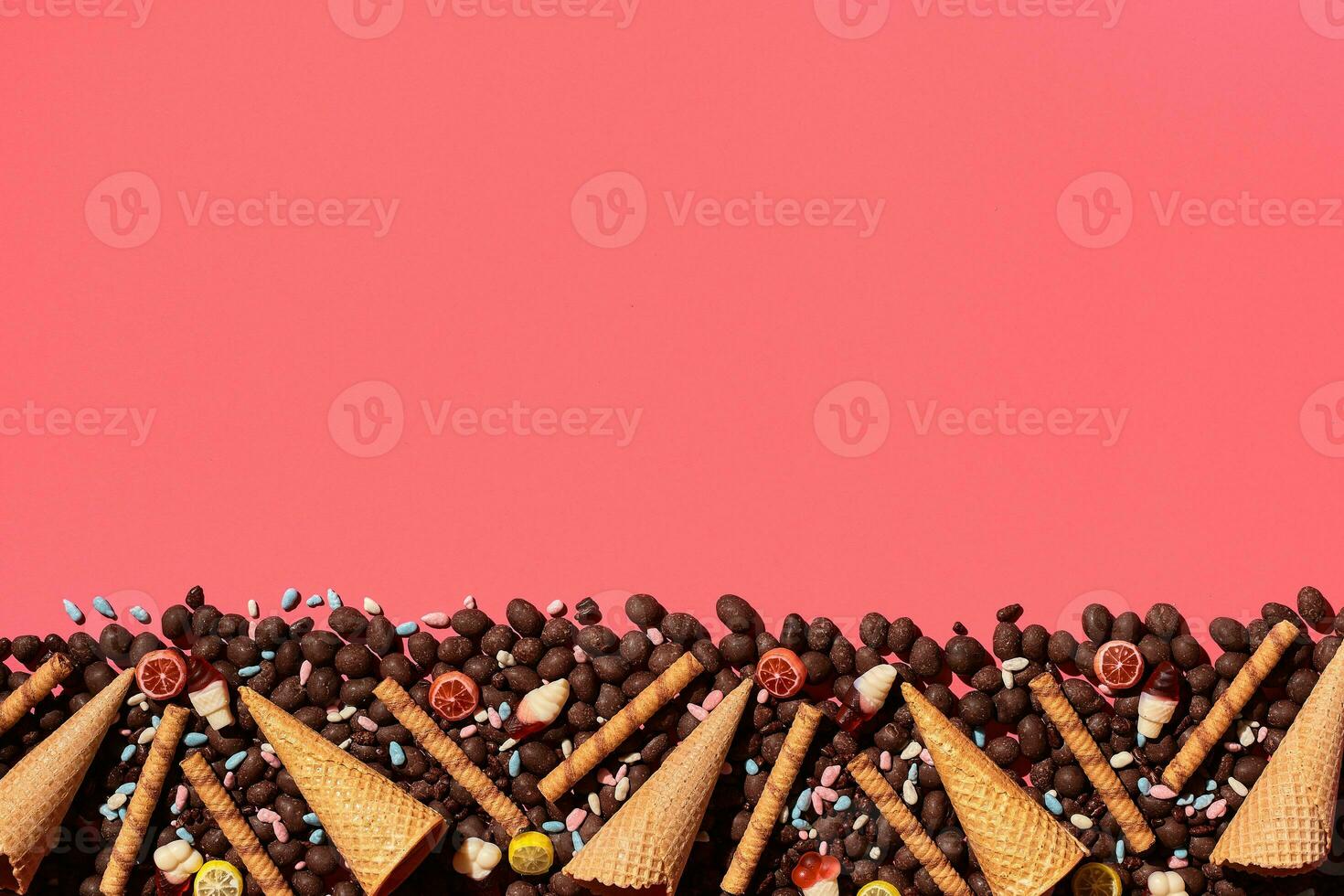 Chocolate dragee and waffle cones placed in fascinating order on coral background, view from above photo
